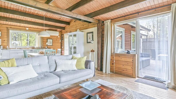 En mysig stuga med träpanel i taket, en grå soffa, ett träbord och en stor skjutdörr i glas som leder ut till en uteplats.