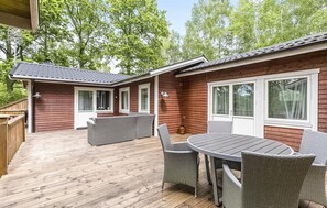 Een houten hut met een terras, buitenmeubels en grote ramen.