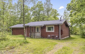 Een klein houten vakantiehuisje met een veranda, één raam en een schoorsteen.