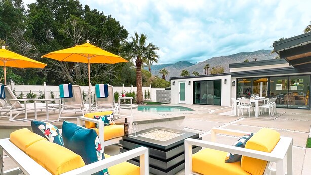 An outdoor patio with yellow and white furniture, a pool, and a modern building in the background.