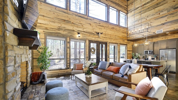 A spacious living area with a stone fireplace, large windows, a wooden ceiling, and a modern kitchen. - Family & Group Cabin w/ Hot Tub & Game Room (Broken Bow)