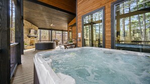 A wooden cabin with a hot tub, large windows, and a stone fireplace. - Family & Group Cabin w/ Hot Tub & Game Room (Broken Bow)