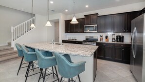 Une cuisine moderne avec des meubles de couleur sombre, un réfrigérateur en acier inoxydable, un four à micro-ondes et un  îlot central en granit avec des tabourets de bar.