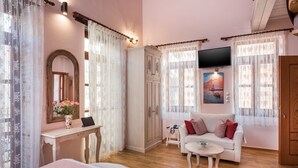 Une pièce confortable avec un lit, un canapé blanc, un bureau agrémenté d’un vase de fleurs, une armoire et un tableau au mur.