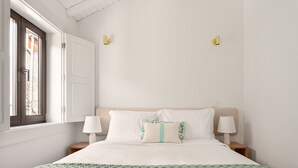Ein ordentlich eingerichtetes Schlafzimmer mit einem Bett, zwei Nachttischlampen und einem Fenster mit Blick.