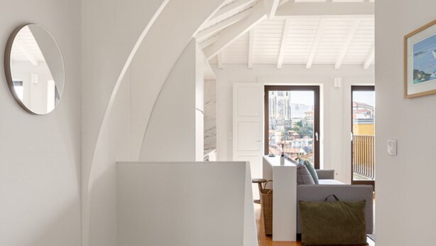 Ein modernes Interieur mit weißer Decke, einem runden Spiegel und Blick auf die Stadt durch ein großes Fenster.