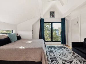 A bedroom with a large bed, a window with curtains, a ceiling fan, and a view of the outside.
