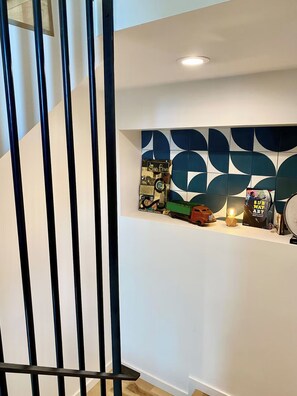 A modern interior with a staircase, a wall-mounted shelf with books and decorative items, and a recessed ceiling light.