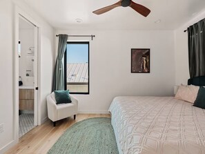 A bedroom with a bed, a chair, a window with curtains, a ceiling fan, and a framed picture on the wall. - Bright and Clean 7BR East Austin Retreat - Sleeps 12 + Private Yard w/ Fire pit (Austin)