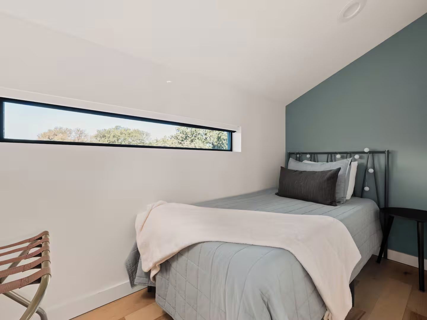 A bedroom with a bed, a window, a chair, and a bedside table.