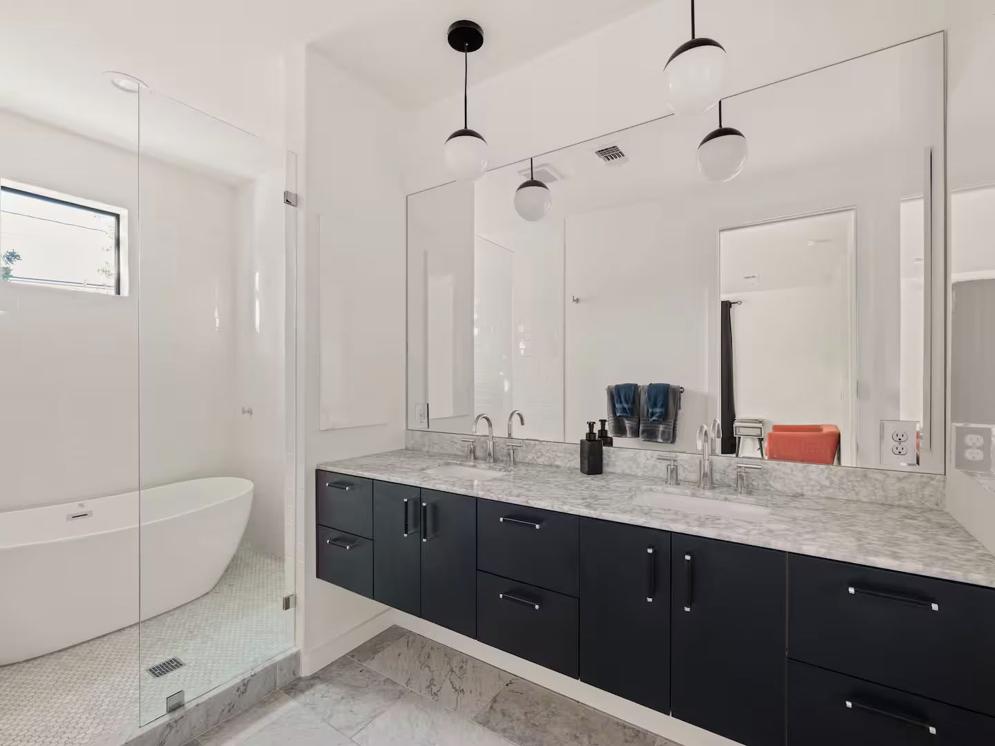 A modern bathroom with a freestanding bathtub, a large mirror, and black cabinets.