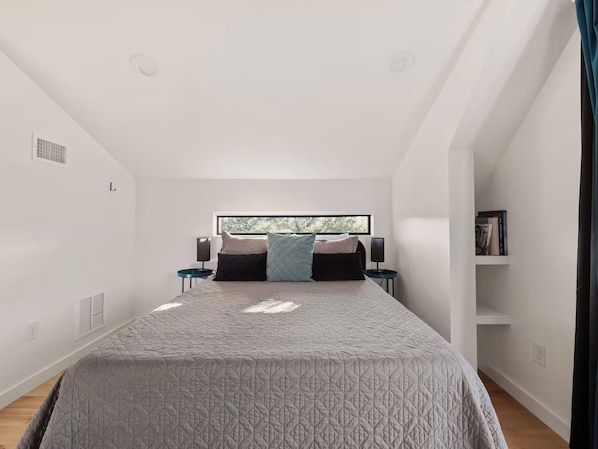 A bedroom with a bed, two bedside tables, a window, and a bookshelf.