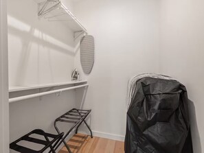 Un petit espace fermé, aménagé pour faire la lessive, comprenant un étendoir, une planche à repasser et un tabouret compact.