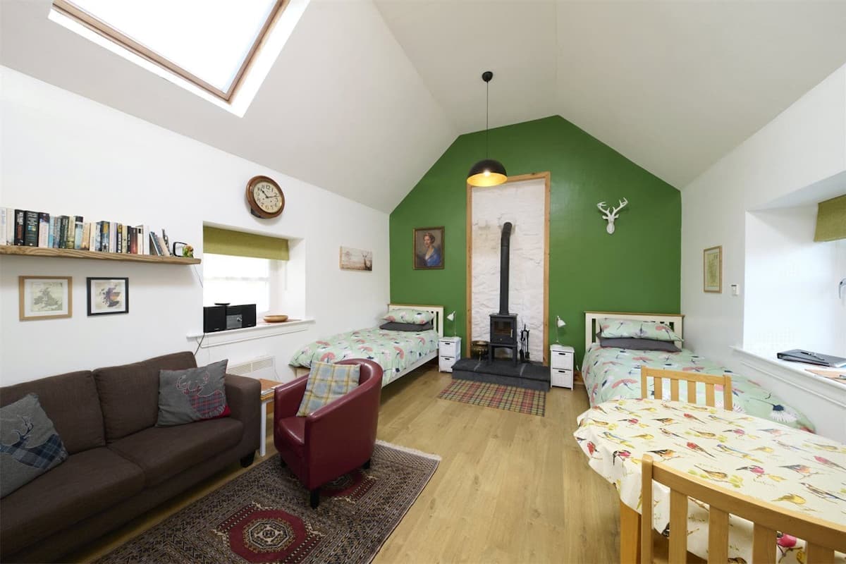 A cozy room with a loft bed, a sofa, a table, and a fireplace.