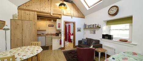 A cozy interior with a dining area, a living room with a sofa, a kitchen, and a loft space with a skylight.