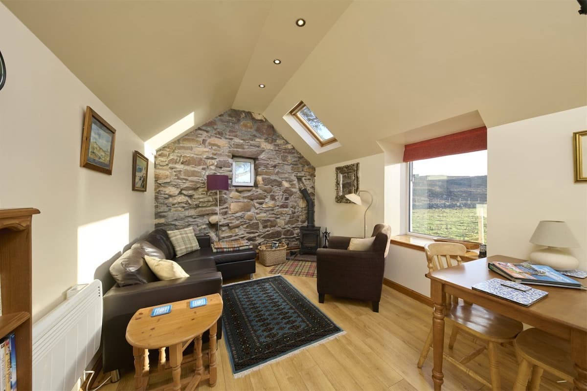 A cozy living room with a stone wall, a fireplace, a sofa, a coffee table, and a view of the outdoors.