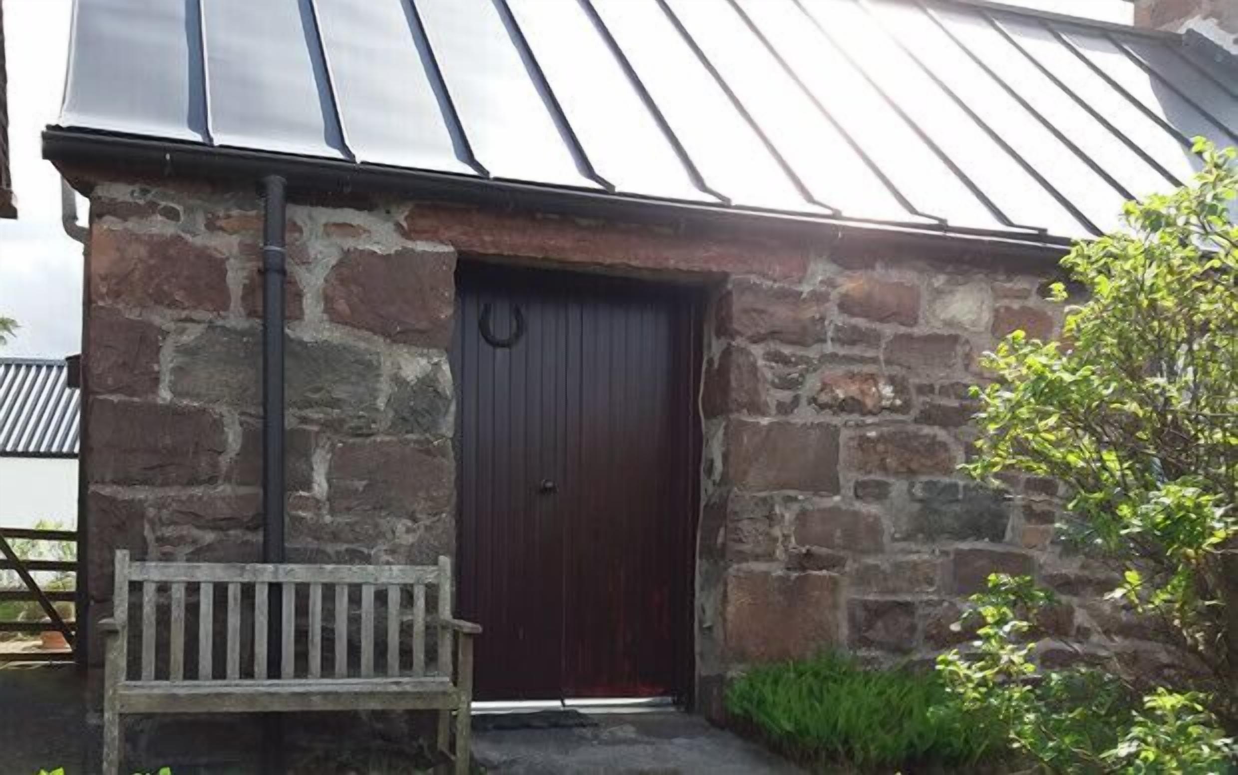 A stone building with a dark wooden door and a metal roof.