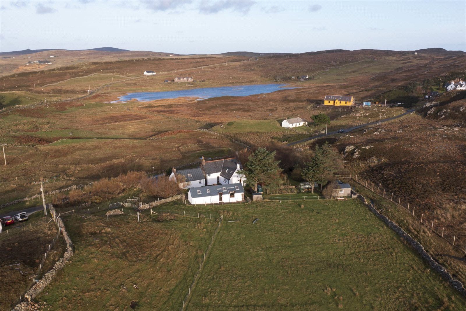 A rural landscape with a house surrounded by fields and a small body of water.