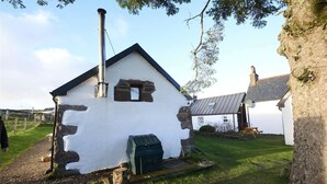 A small, white building with a stone foundation, a chimney, and a small window. - The Smithy House & Cottages (Stoer)