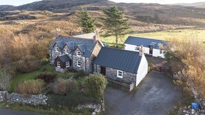 A stone house with multiple rooms, a fenced yard, and a view of rolling hills in the background. - The Smithy House & Cottages (Stoer)
