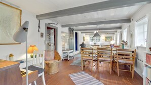 A spacious dining area with a high ceiling, a dining table with chairs, a wicker chair, a lamp, and a bookshelf. - 3 bedroom stunning home in Rømø (Rømø)