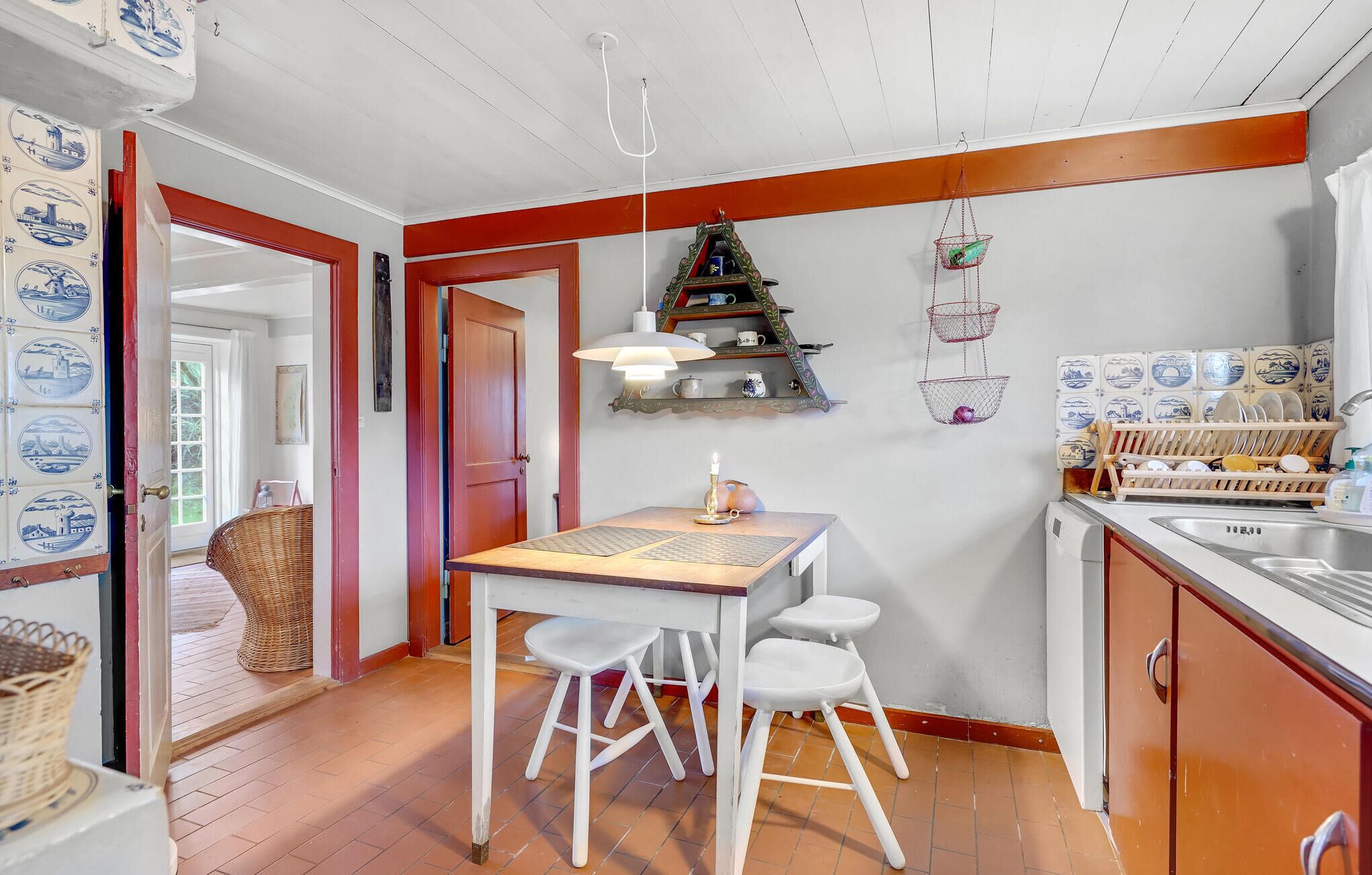 A kitchen with a wooden table, white chairs, a hanging light fixture, and a dish rack.
