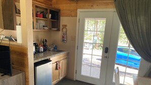 A compact kitchen with wooden cabinets, a built-in dishwasher, a sink, and a window with a view of parked cars and trees.