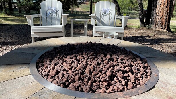 Two Adirondack chairs with "Mrs." and "Mr." engraved on them, placed on a stone patio with a circular fire pit in the center.