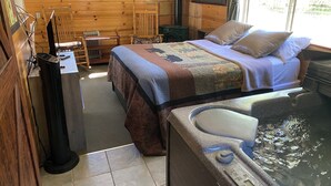 A cozy cabin room with a bed, a small table, a chair, a heater, and a hot tub.
