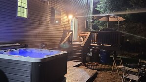 Un bain à remous dans un jardin, avec une terrasse en bois et un espace salon abrité.