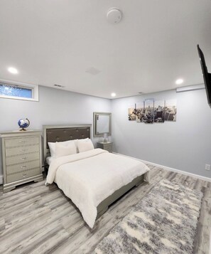 Une chambre à coucher comprenant un lit, une commode, une table de chevet et une œuvre d’art représentant un paysage urbain accrochée au mur.
