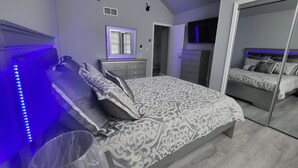 Une chambre à coucher avec un grand lit, une commode, un miroir et un éclairage décoratif à LED.