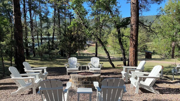 Un espace de détente circulaire, avec des fauteuils Adirondack et un foyer central, le tout entouré d’arbres.