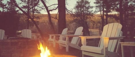 A fire pit with chairs around it, set in a wooded area.