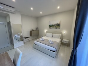 A modern hotel room with a large bed, a bedside table, a mirror, and a painting on the wall. - Quintus Luxury Suites (Rome)