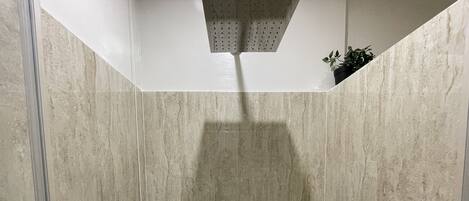 A shower with a rain showerhead, tiled walls, and a small potted plant in the corner.