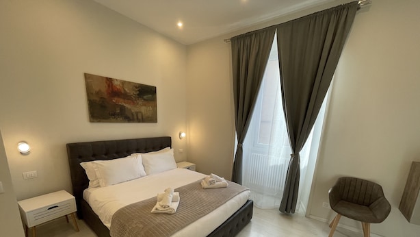 A modern hotel room with a large bed, a bedside table, a chair, and a painting on the wall. - Quintus Luxury Suites (Rome)