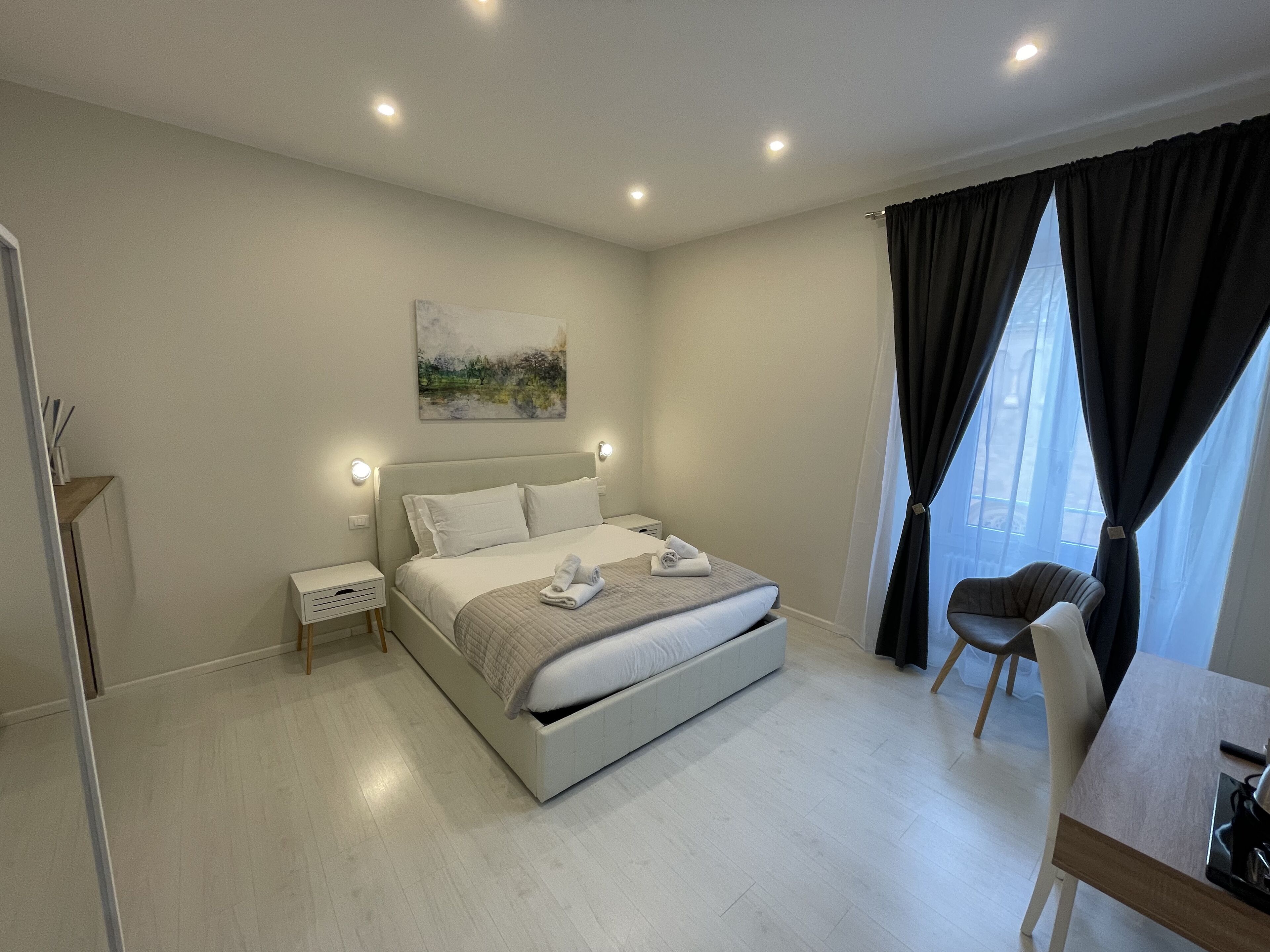 A modern bedroom with a large bed, bedside tables, a chair, and a painting on the wall.