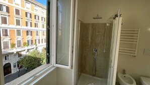 A bathroom with a glass-enclosed shower, a bidet, and a window overlooking a street. - Quintus Luxury Suites (Rome)
