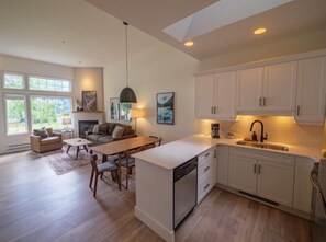 Enjoy a cozy atmosphere with a dining area, sofa, and fireplace, plus a functional kitchen with white cabinetry and sink.
