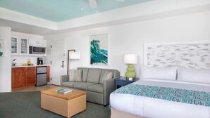 Habitación de hotel con cama, sofá, mesa de comedor, zona de cocina y una obra de arte grande en la pared.
