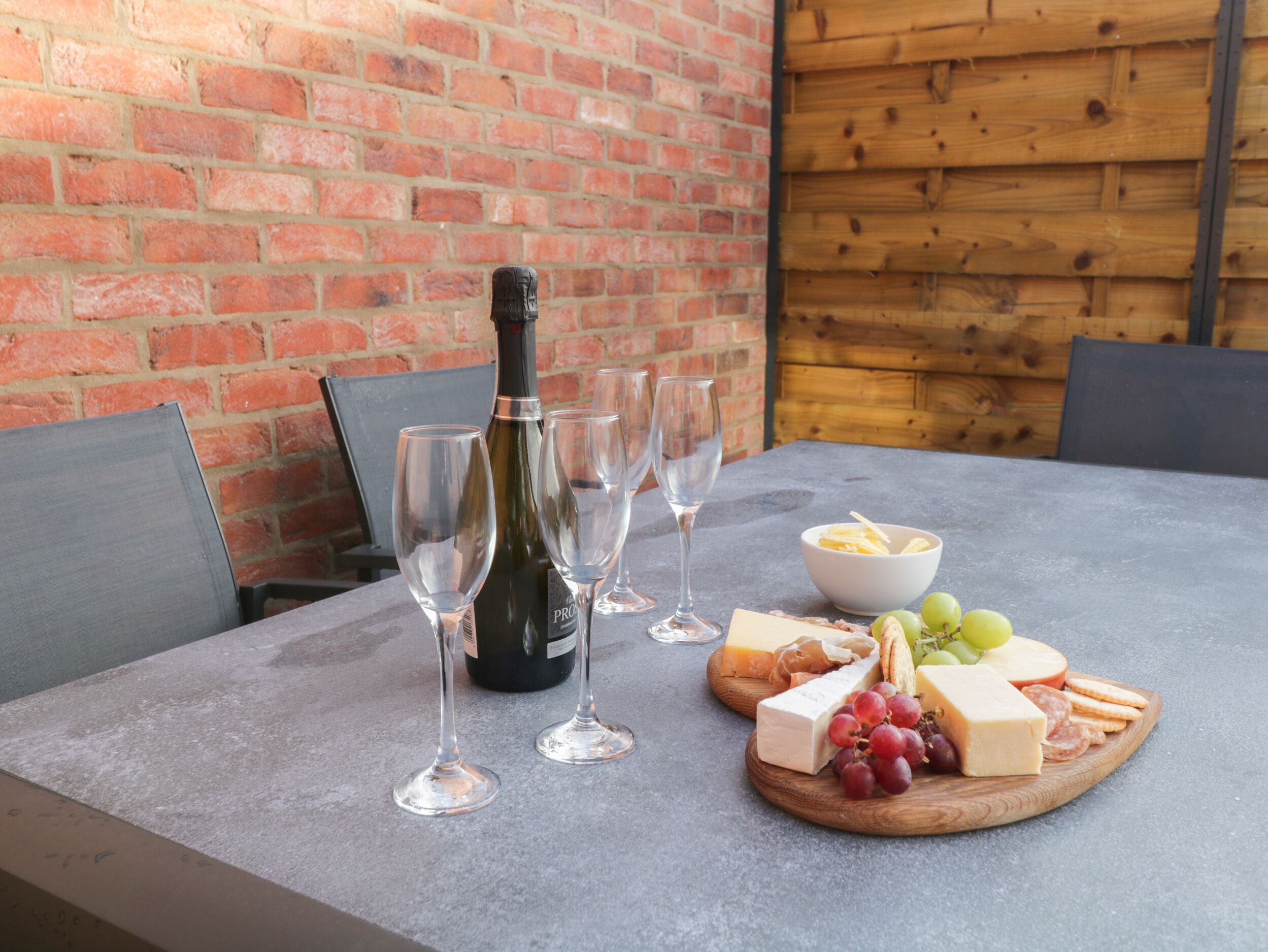 Una mesa con una botella de vino, copas, queso, uvas y galletas.