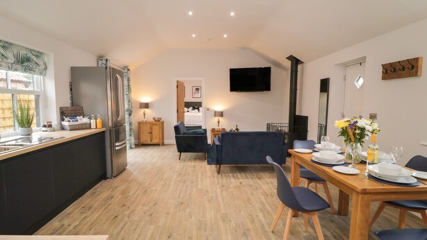 A modern kitchen with a dining area, a sofa, and a TV mounted on the wall. - Bracken Cottage (York)