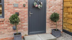 A brick cottage with a dark grey door, a small sign reading "Bracken Cottage", and two potted plants on either side of the entrance. - Bracken Cottage (York)