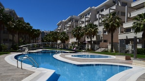 Un hôtel moderne doté d’une piscine centrale, de palmiers et surplombant un ciel d’un bleu éclatant.