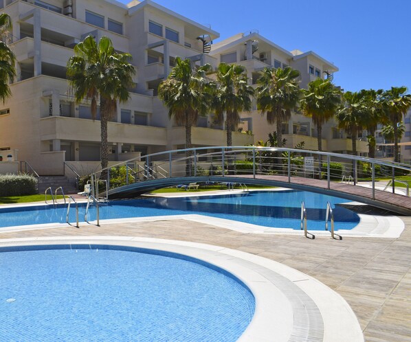 Una piscina con un puente, palmeras y un edificio de varios pisos al fondo.