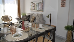 Un coin repas avec une table en verre, des chaises, ainsi qu’une variété d’assiettes et de verres. On y trouve également un canapé et un tableau accroché au mur.