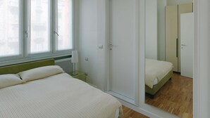 A bedroom with a bed, a nightstand, a lamp, a mirror, and a door. - 50m2 Apartment Near Milano Centrale (Milan)