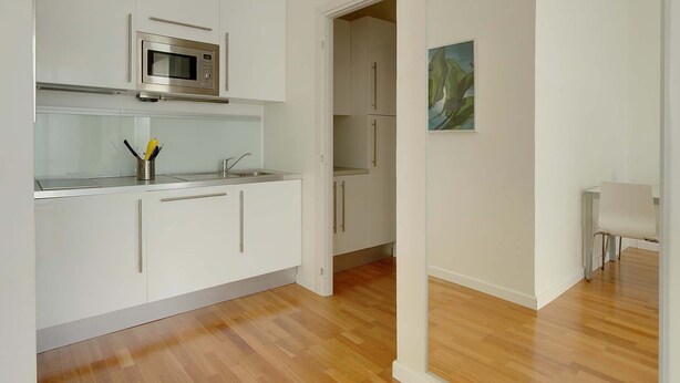 A modern kitchen with white cabinetry, a stainless steel microwave, and a wooden floor. - 50m2 Apartment Near Milano Centrale (Milan)