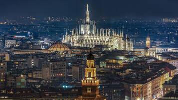 Une vue nocturne d’une ville, avec des bâtiments illuminés et une imposante cathédrale en arrière-plan.